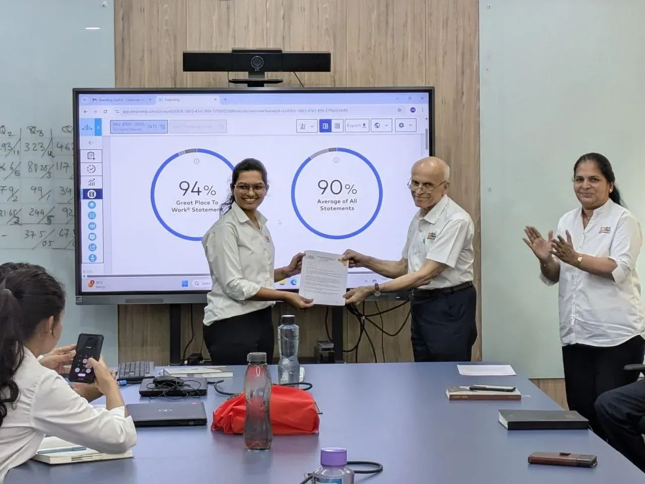 An employee receiving her appreciation letter while the engagement survey results of 94 percent and 90 percent are displayed on screen
