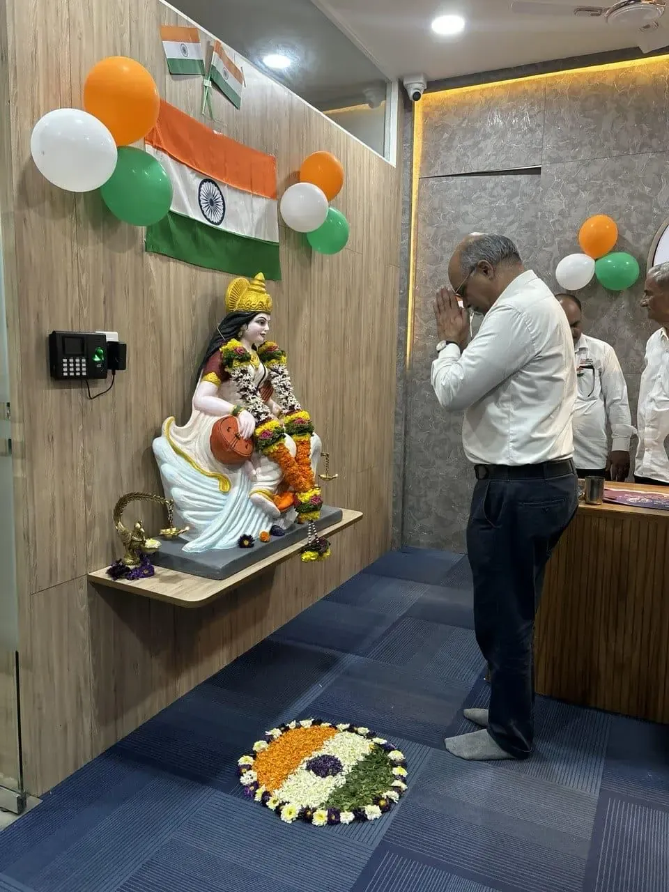 A senior colleague with folded hands before the Saraswati idol under the national flag on Republic Day