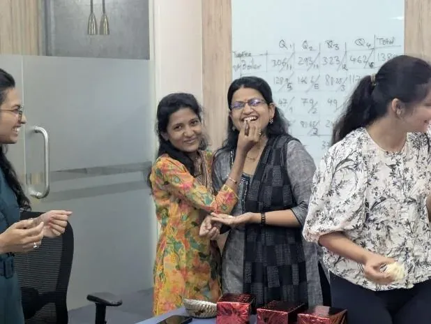 Women colleagues sharing sweets and laughing together during the Women's Day celebration