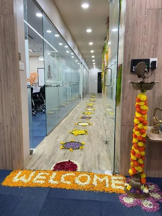 Floral rangoli and a marigold WELCOME mat leading down the new office corridor past the glass-walled design bay