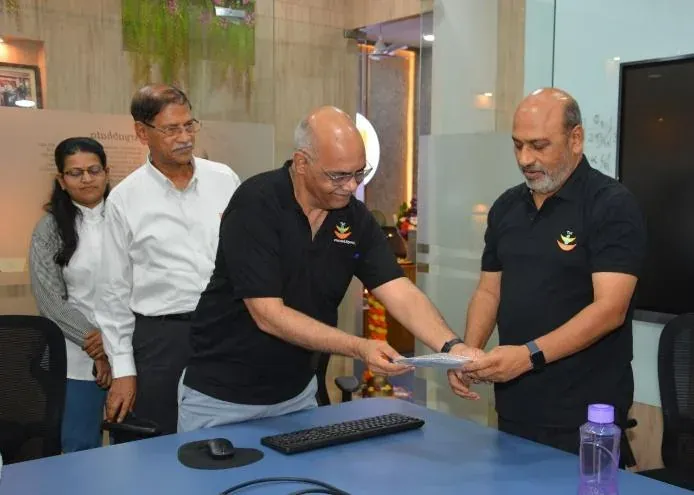 Bagwe Sir handing over an inauguration memento to a colleague across the conference table, with the leadership team looking on