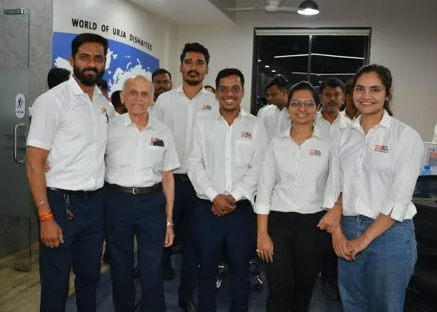 Urja-Disha engineers standing with a TLC guest in front of the World of Urja Dishaites wall map