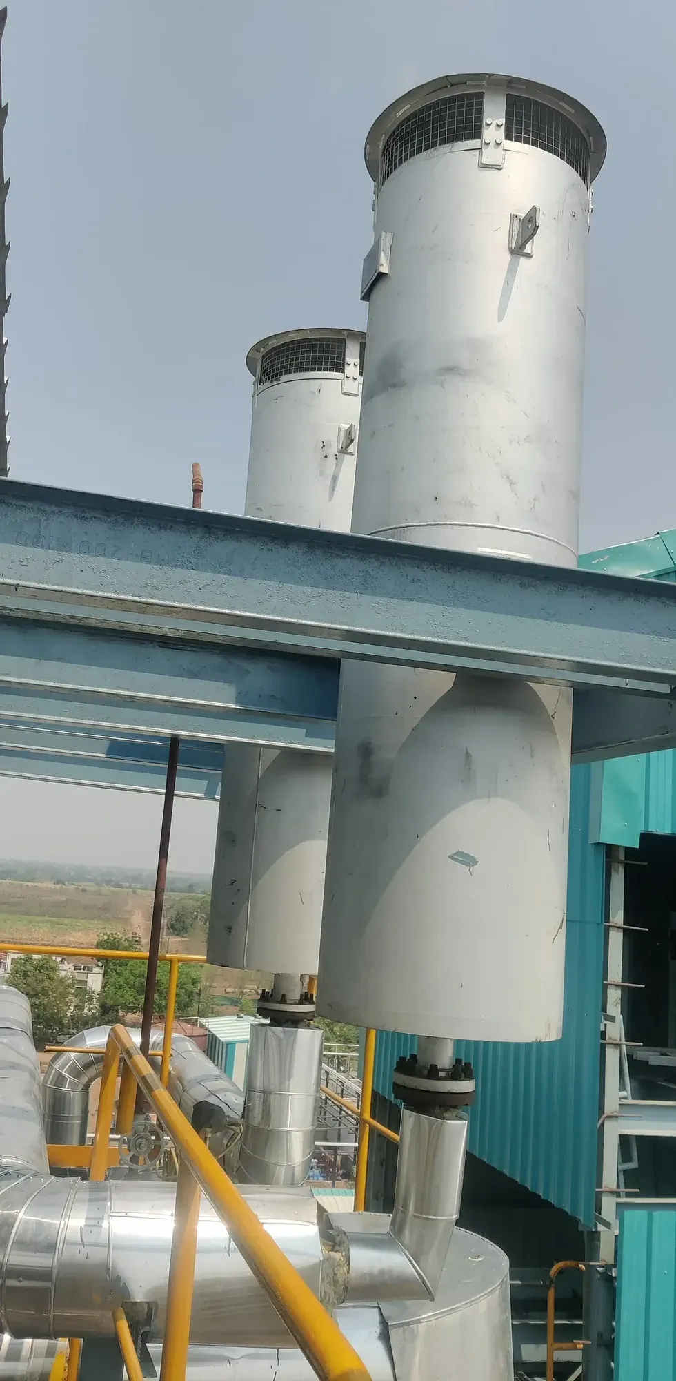 Two steam blow-off silencer stacks with mesh vents mounted above insulated steam piping at a plant