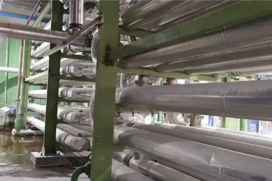 Rows of pipe-in-pipe heat exchanger runs stacked on green steel supports inside a process plant